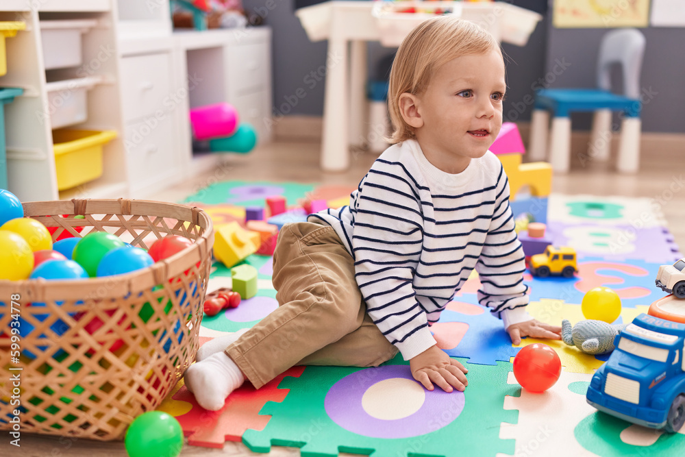 Fototapeta premium Adorable caucasian boy playing with balls sitting on floor at kindergarten