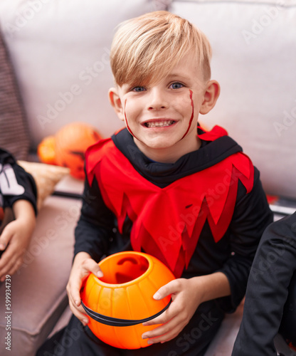 Adorable caucasian boy wearing halloween costume holding pumpkin basket at home