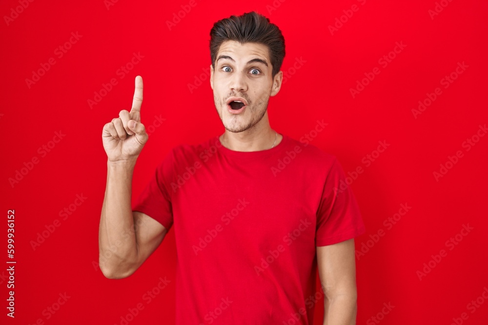 Young hispanic man standing over red background pointing finger up with successful idea. exited and happy. number one.