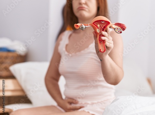 Young woman suffering for menstrual pain holding anatomical model of uterus at bedroom