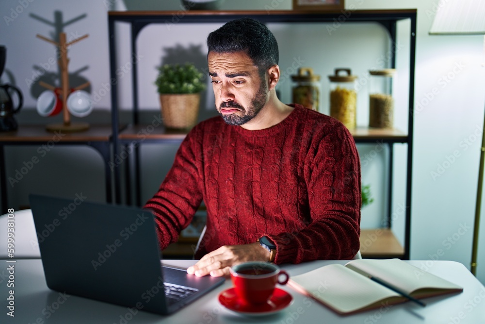 Young hispanic man with beard using computer laptop at night at home depressed and worry for distress, crying angry and afraid. sad expression. Young hispanic man with beard using computer laptop at night at home depressed and worry for distress, crying angry and afraid. sad expression.