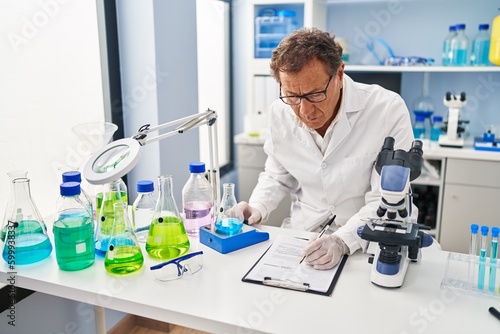 Middle age man wearing scientist uniform measuring test tube writing on clipboard at laboratory © Krakenimages.com