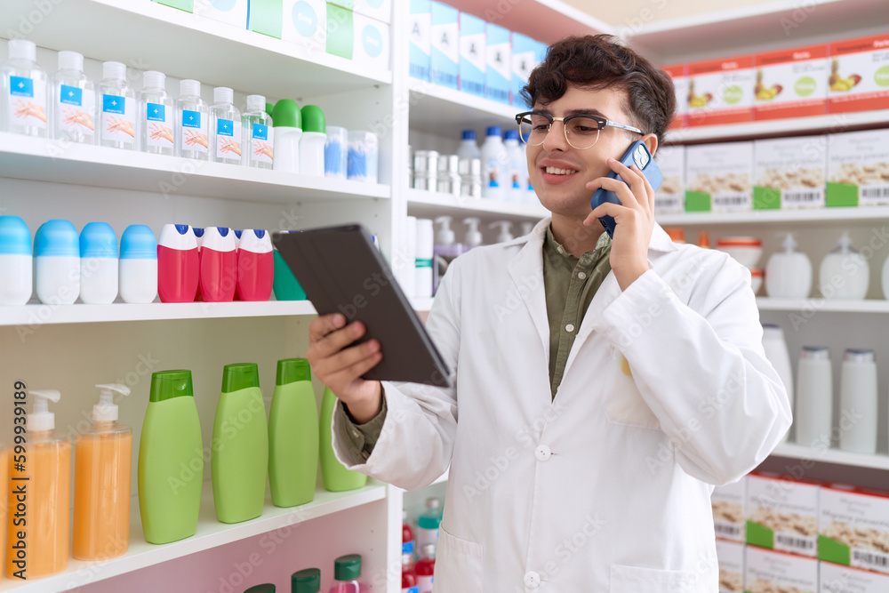Non binary man pharmacist using touchpad talking on smartphone at pharmacy