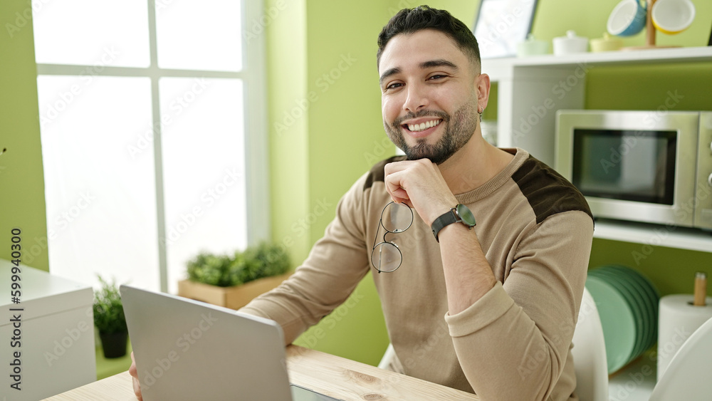 Young arab man using laptop holding glasses at home Young arab man using laptop holding glasses at home