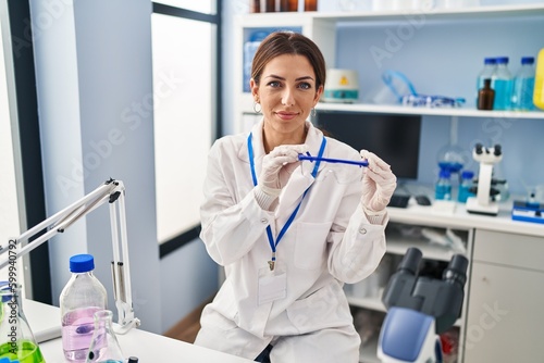 Young brunette woman working at scientist laboratory wearing safety glasses relaxed with serious expression on face. simple and natural looking at the camera.