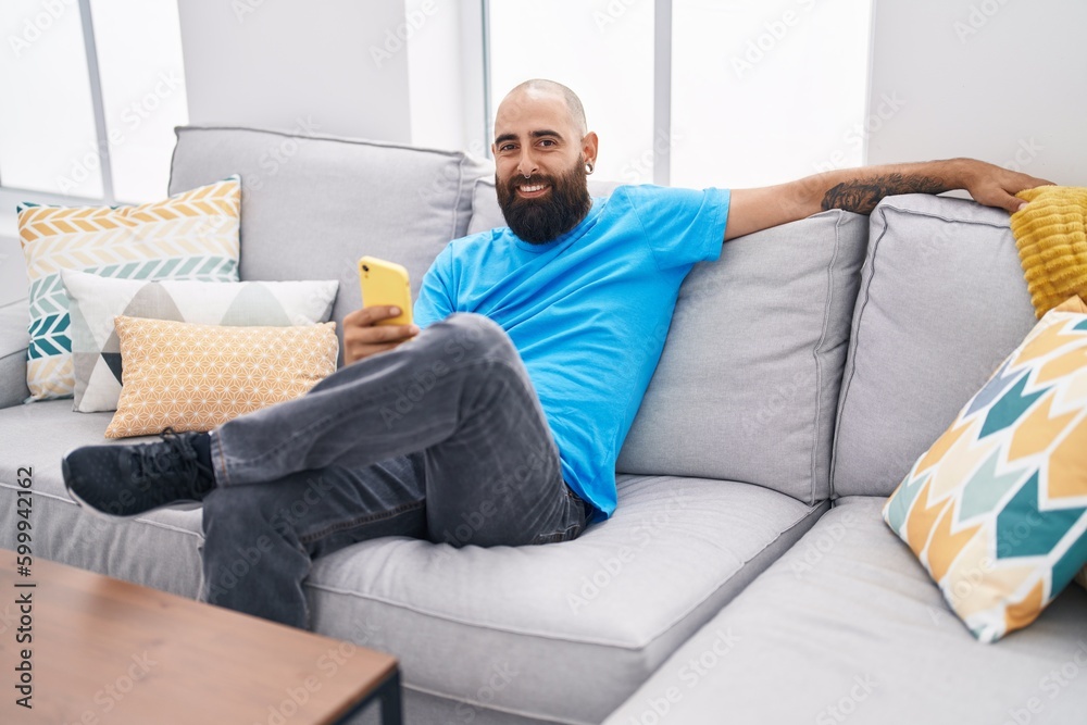 Young bald man using smartphone sitting on sofa at home