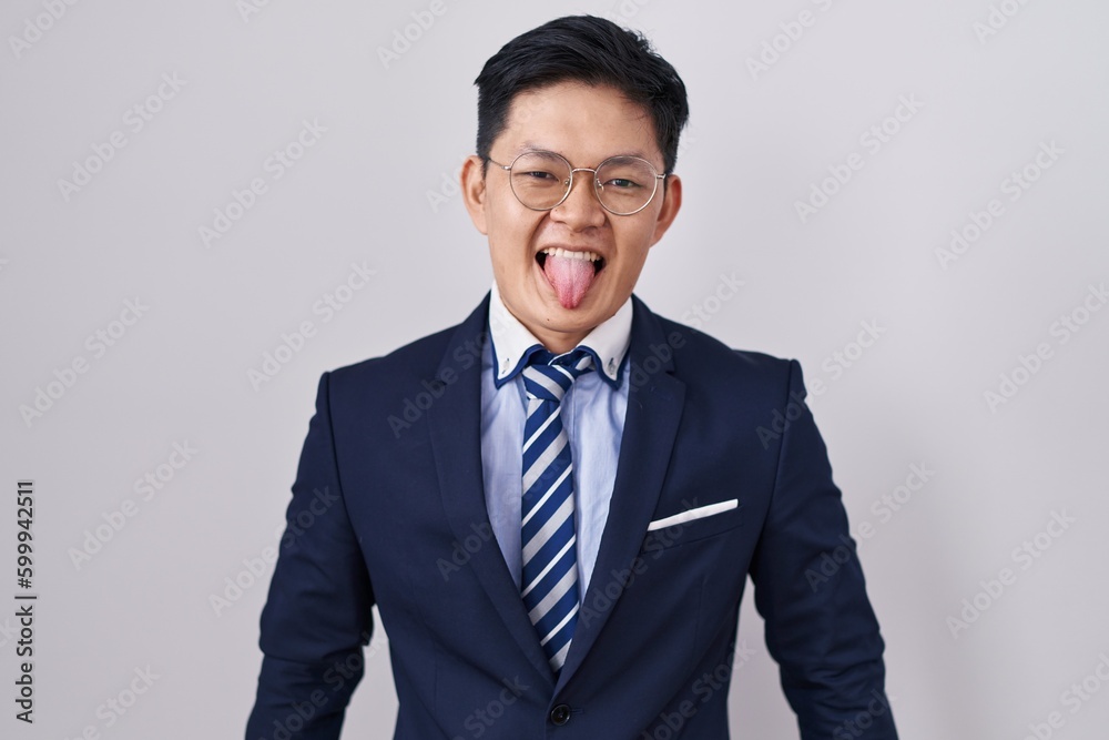 Young asian man wearing business suit and tie sticking tongue out happy with funny expression. emotion concept. Young asian man wearing business suit and tie sticking tongue out happy with funny expression. emotion concept.