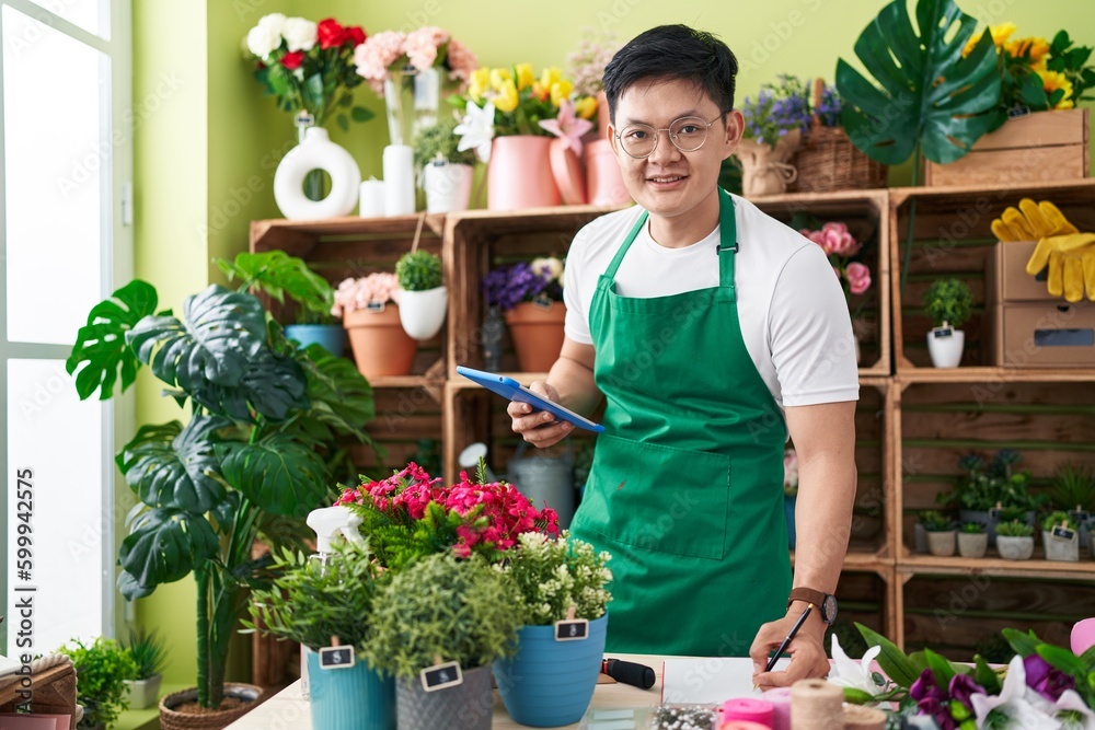 Young chinese man florist using touchpad writing on notebook at flower shop Young chinese man florist using touchpad writing on notebook at flower shop