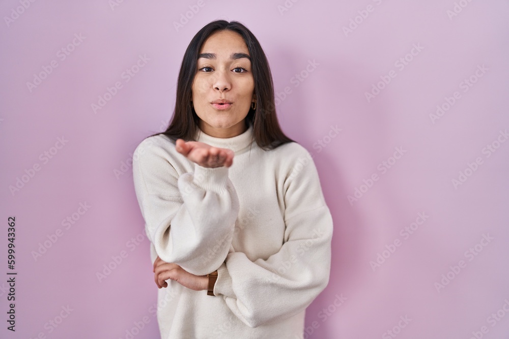 Young south asian woman standing over pink background looking at the camera blowing a kiss with hand on air being lovely and sexy. love expression. Young south asian woman standing over pink background looking at the camera blowing a kiss with hand on air being lovely and sexy. love expression.
