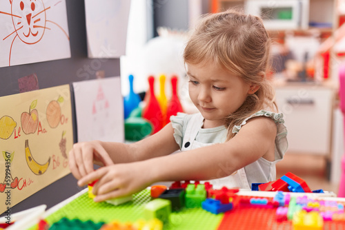 Adorable blonde girl playing with construction blocks sitting on table at kindergarten