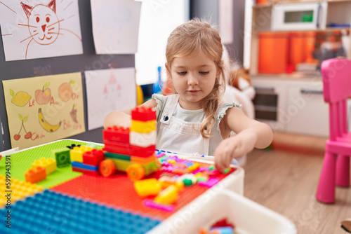 Adorable blonde girl playing with construction blocks sitting on table at kindergarten