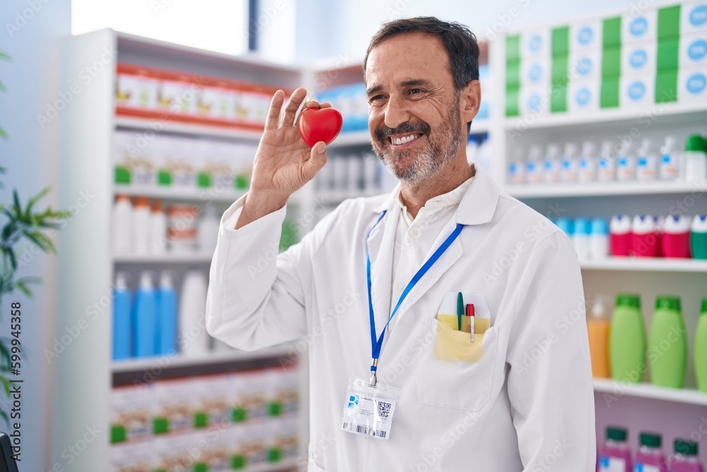 Middle age man pharmacist smiling confident holding heart at pharmacy