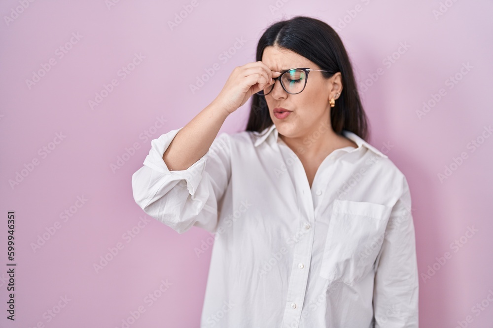 Young brunette woman standing over pink background tired rubbing nose and eyes feeling fatigue and headache. stress and frustration concept. Young brunette woman standing over pink background tired rubbing nose and eyes feeling fatigue and headache. stress and frustration concept.