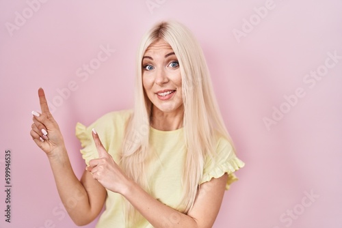 Caucasian woman standing over pink background pointing aside worried and nervous with both hands  concerned and surprised expression