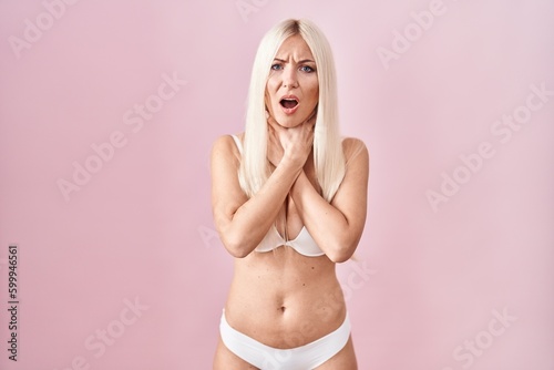 Caucasian woman wearing lingerie over pink background shouting and suffocate because painful strangle. health problem. asphyxiate and suicide concept.