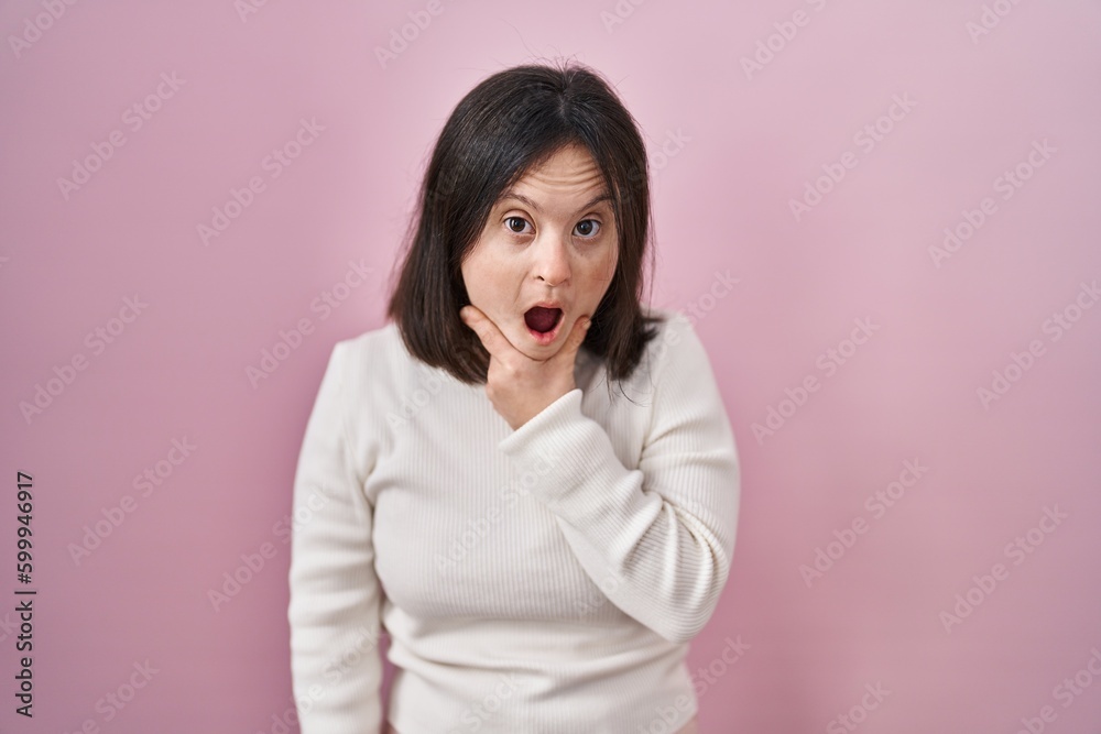 Woman with down syndrome standing over pink background looking fascinated with disbelief, surprise and amazed expression with hands on chin Woman with down syndrome standing over pink background looking fascinated with disbelief, surprise and amazed expression with hands on chin