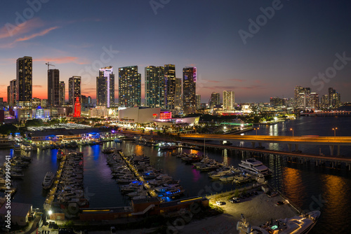 Aerial view of yachts in Miami marina at Bayside Marketplace with reflections in Biscayne Bay water and high illuminated skyscrapers of Brickell, city's financial center at night