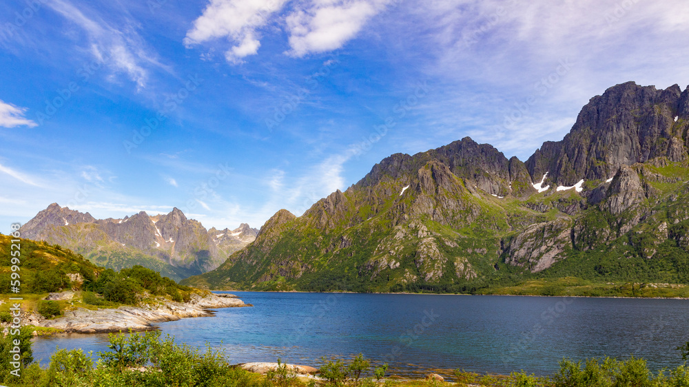 magical mountain scenery behind a lake on the archipelago den lofoten in norway under a slightly cloudy blue sky