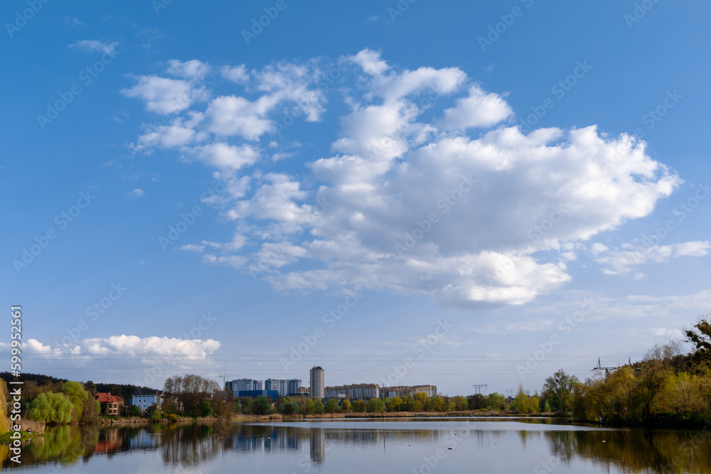 Lake under blue cloudy sky. Lake surrounded by trees and houses