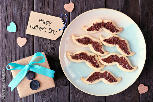 Fun Fathers Day mustache cookies. Top down view with gift greeting card over a dark wood background.