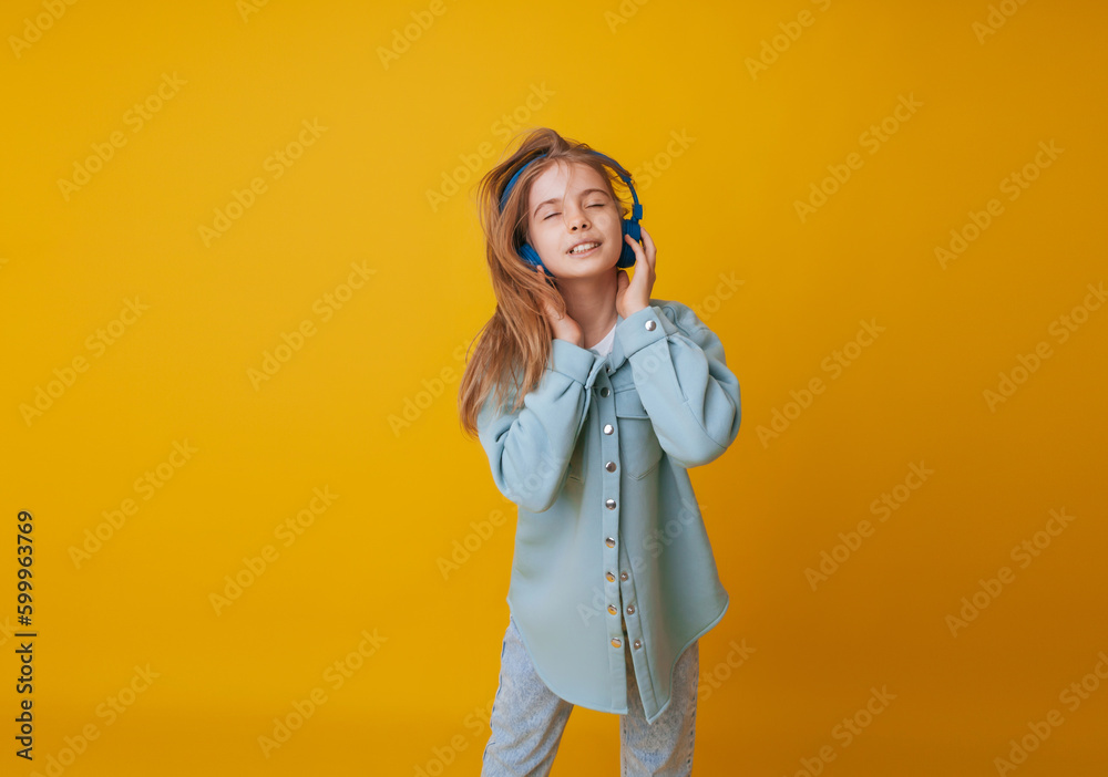 A young girl 11-13 years old in headphones listens to music and dances in the studio on a yellow background