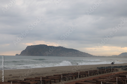 Fototapeta Naklejka Na Ścianę i Meble -  Thunderstorm over the Mediterranean Sea on a windy summer evening. Impressive waves, the sky is covered with dark clouds. Sandy beach, wet beach chairs.