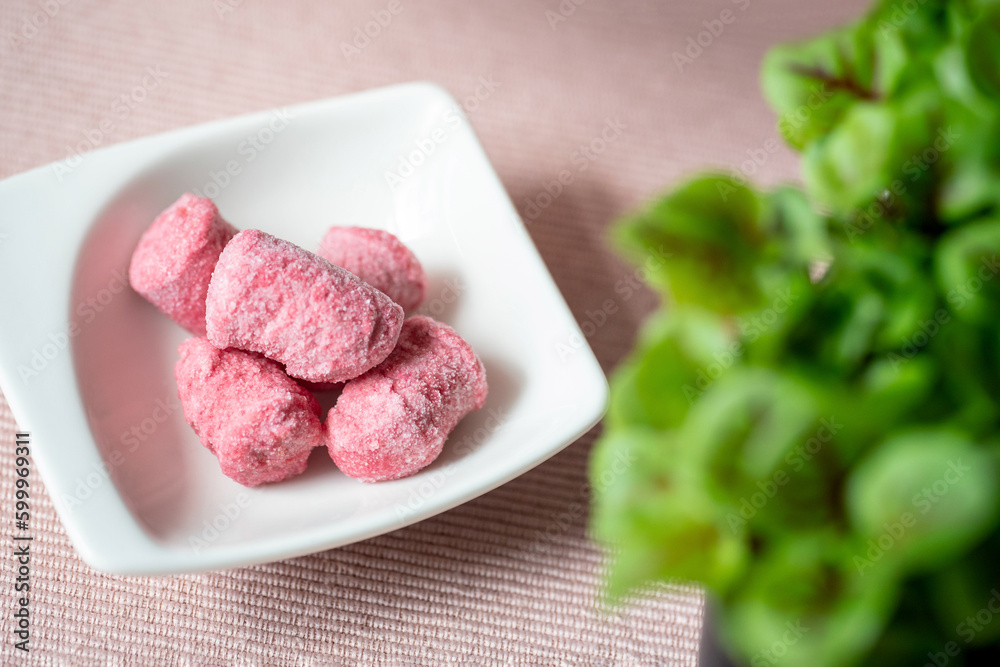 Still frozen pink (beetroot) gnocchi in a white small bowl on the pink cloth. Baby swiss chard in the backgrond.