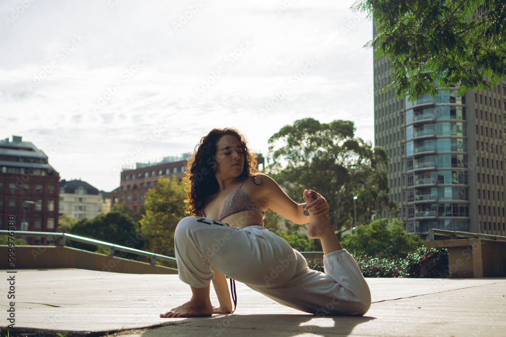 young latin woman in a city park stretching, doing hip opening Eka Pada Rajakapotasana exercise or One Legged King Pigeon pose young latin woman in a city park stretching, doing hip opening Eka Pada Rajakapotasana exercise or One Legged King Pigeon pose