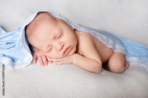 newborn baby sleeps on a white blanket under a blue blanket. Healthy newborn child take a nap asleep. Closeup portrait of happy baby sleeping sweet dream on bed
