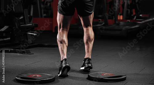 Trained man's legs with muscular calves in sneakers in fitness training gym