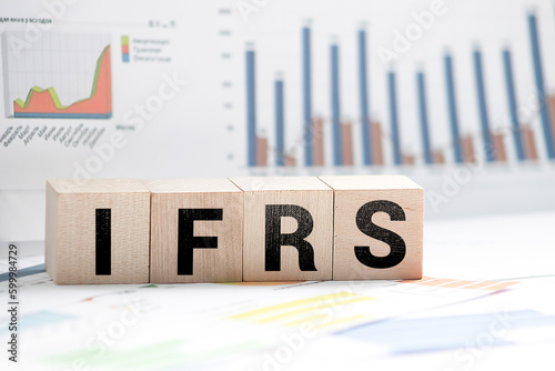 wooden cubes with the word IFRS on financial background with chart, calculator, pen and glasses, business concept