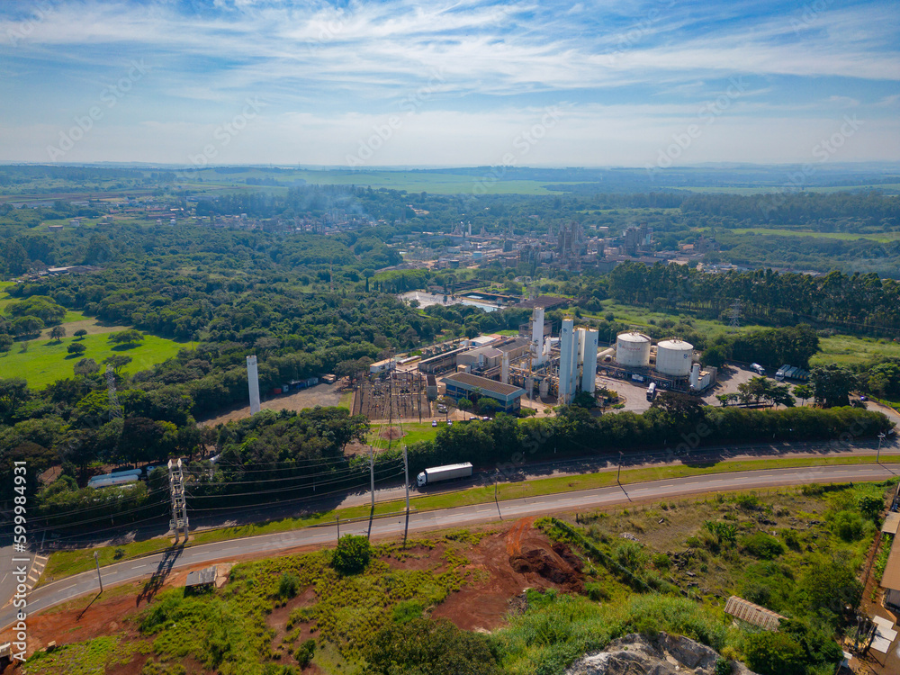 Naklejka premium Aerial image of chemical industry. Large structure of pipelines and warehouses with movement of cargo trucks. Industry surrounded by vast vegetation and trees. Located in Brazil, city of Paulínia.