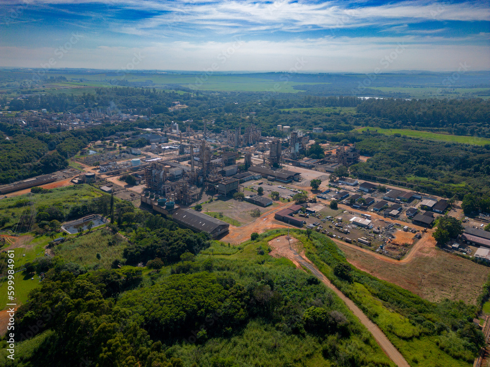 Aerial image of chemical industry. Large structure of pipelines and warehouses with movement of cargo trucks. Industry surrounded by vast vegetation and trees. Located in Brazil, city of Paulínia. Aerial image of chemical industry. Large structure of pipelines and warehouses with movement of cargo trucks. Industry surrounded by vast vegetation and trees. Located in Brazil, city of Paulínia.