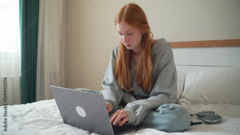 Teenage red head girl using laptop at home on bed. Young woman Studying, typing working with gadget, distance learning. Freelancer, student session, online education. Internet, technology Teenage red head girl using laptop at home on bed. Young woman Studying, typing working with gadget, distance learning. Freelancer, student session, online education. Internet, technology
