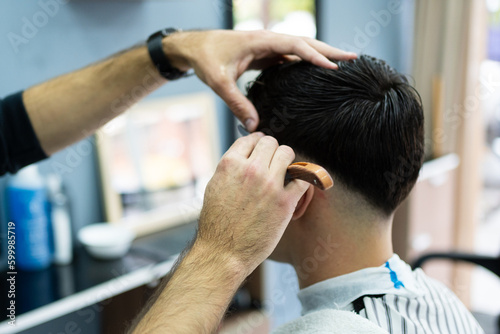 Hairdresser's hands cutting a male customer's hair with a razor.
