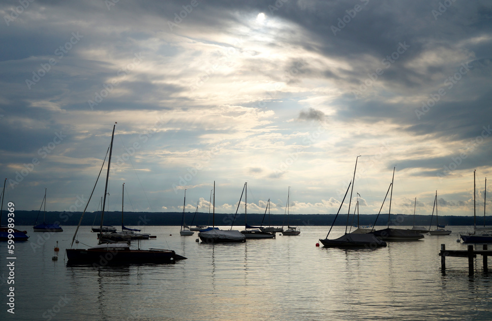 a tranquil scenery with sailing boats resting on calm lake Ammersee in Herrsching on an overcast serene evening in spring (Herrsching on Ammersee, Bavaria, Germany)