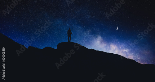 Silhouette of man in mountains under beautiful starry sky with crescent moon at night, banner design