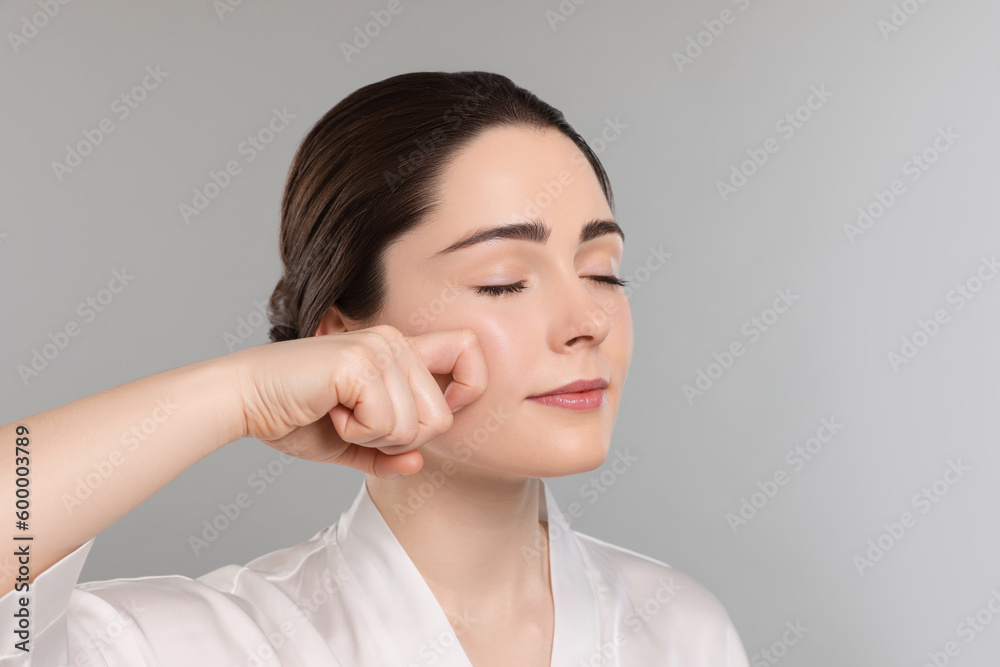 Young woman massaging her face on grey background. Space for text Young woman massaging her face on grey background. Space for text