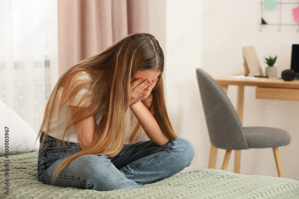 Unhappy teenage girl covering face with hands on bed at home Unhappy teenage girl covering face with hands on bed at home