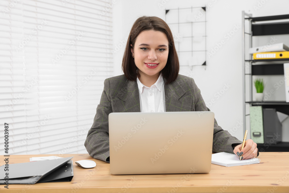 Happy young intern working with laptop at table in modern office Happy young intern working with laptop at table in modern office