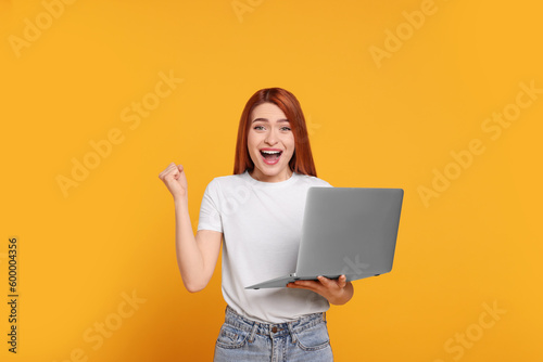Happy young woman with laptop on yellow background