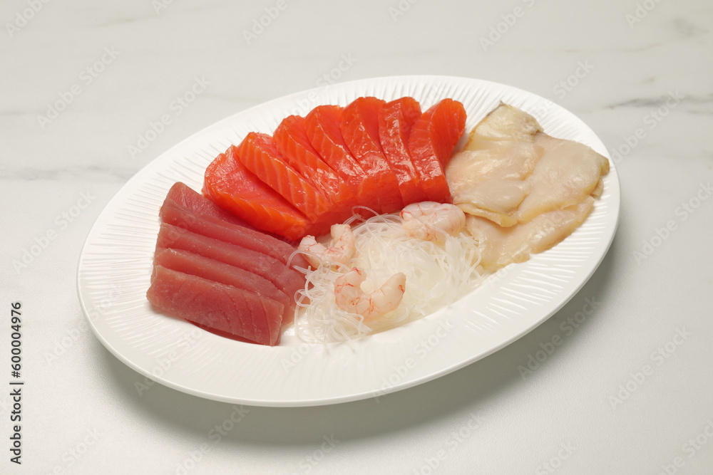 Tasty salmon slices, shrimp, funchosa and tuna on white marble table. Delicious sashimi dish