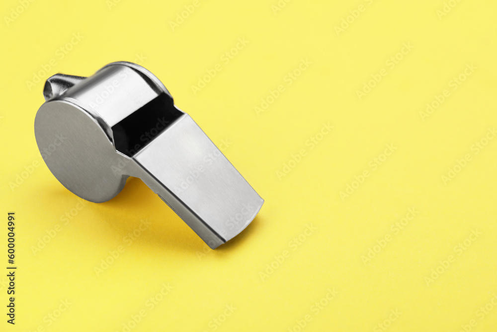 One metal whistle on yellow background, closeup and space for text