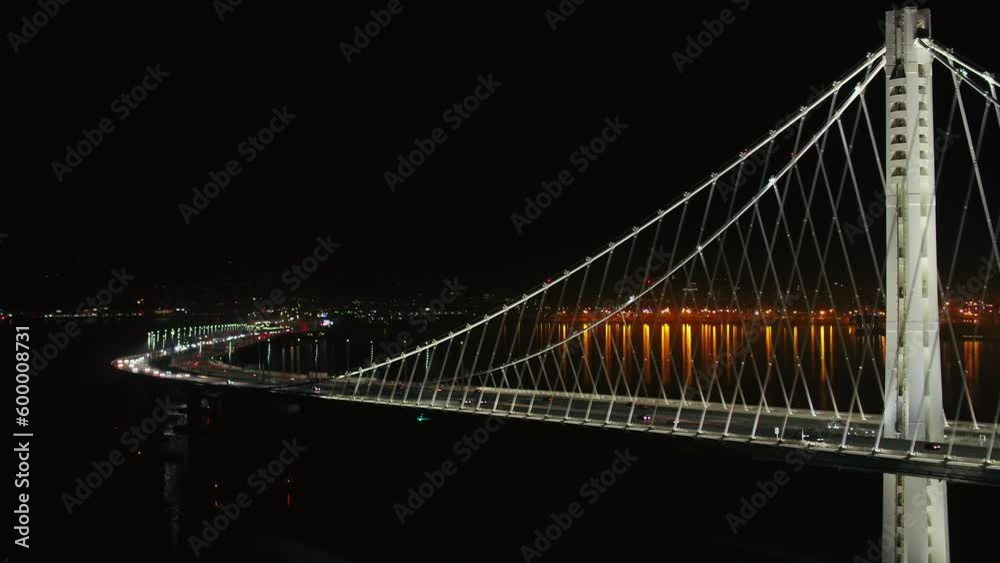 Aerial Panning Shot Of Vehicles On Illuminated Oakland Bay Bridge, Drone Flying Near Famous Landmark On Sea Against Sky At Night - San Francisco, California
