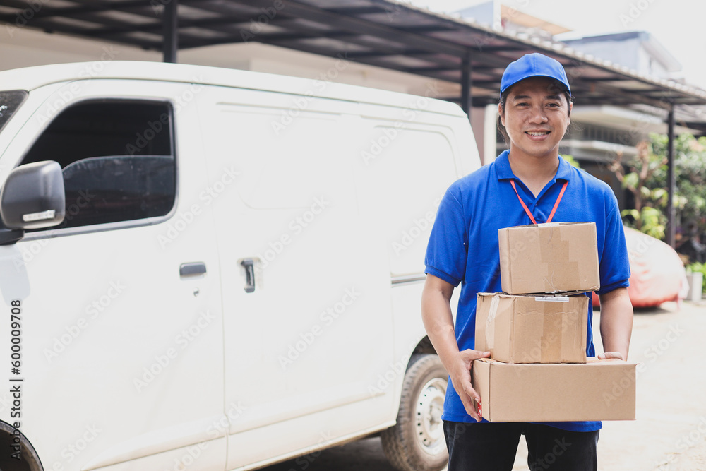 Smiling deliveryman in blue uniform holds pile of boxes out of shipping van. Smiling deliveryman in blue uniform holds pile of boxes out of shipping van.
