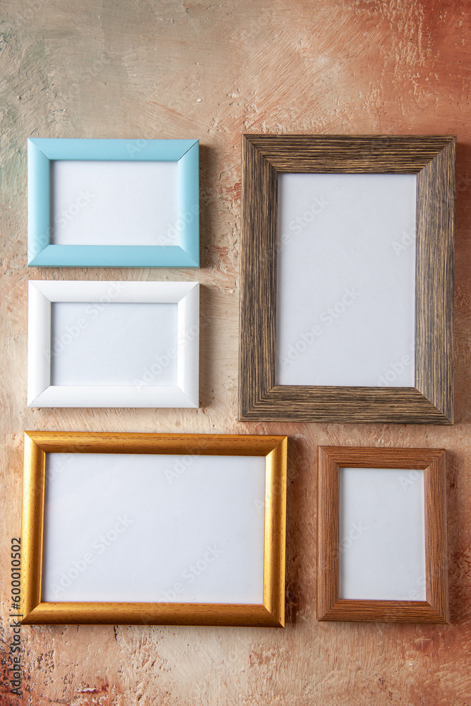 Vertical view of wooden photo frames in different sizes hung on side by side on mix color wall with free space Vertical view of wooden photo frames in different sizes hung on side by side on mix color wall with free space