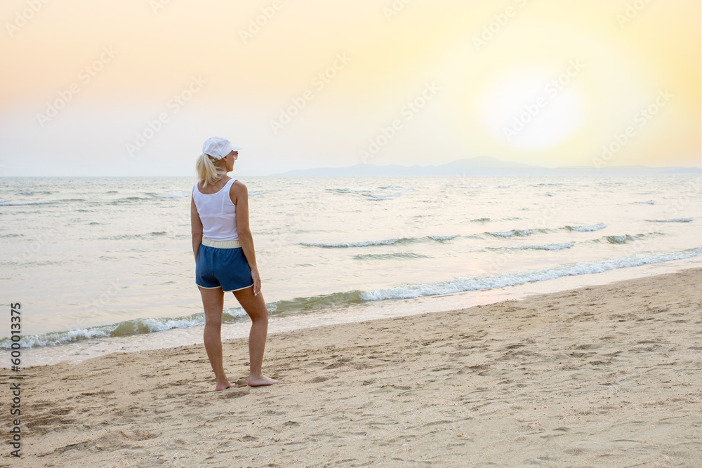  woman standing and watching sun on the beach at sunset.