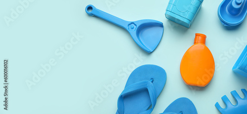 Sunscreen cream, beach toys and flip-flops for child on light blue background with space for text