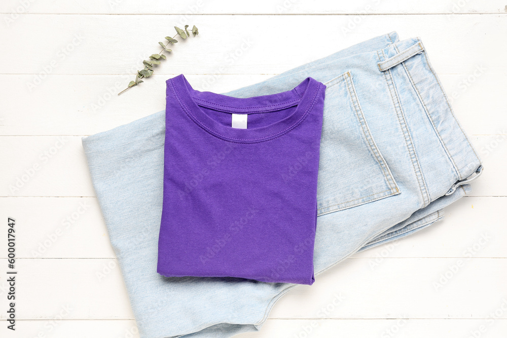 Folded t-shirt and jeans with eucalyptus branch on white wooden background Folded t-shirt and jeans with eucalyptus branch on white wooden background