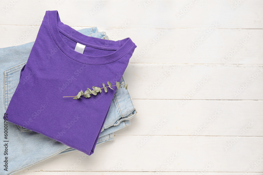 Folded t-shirt and jeans with eucalyptus branch on white wooden background Folded t-shirt and jeans with eucalyptus branch on white wooden background